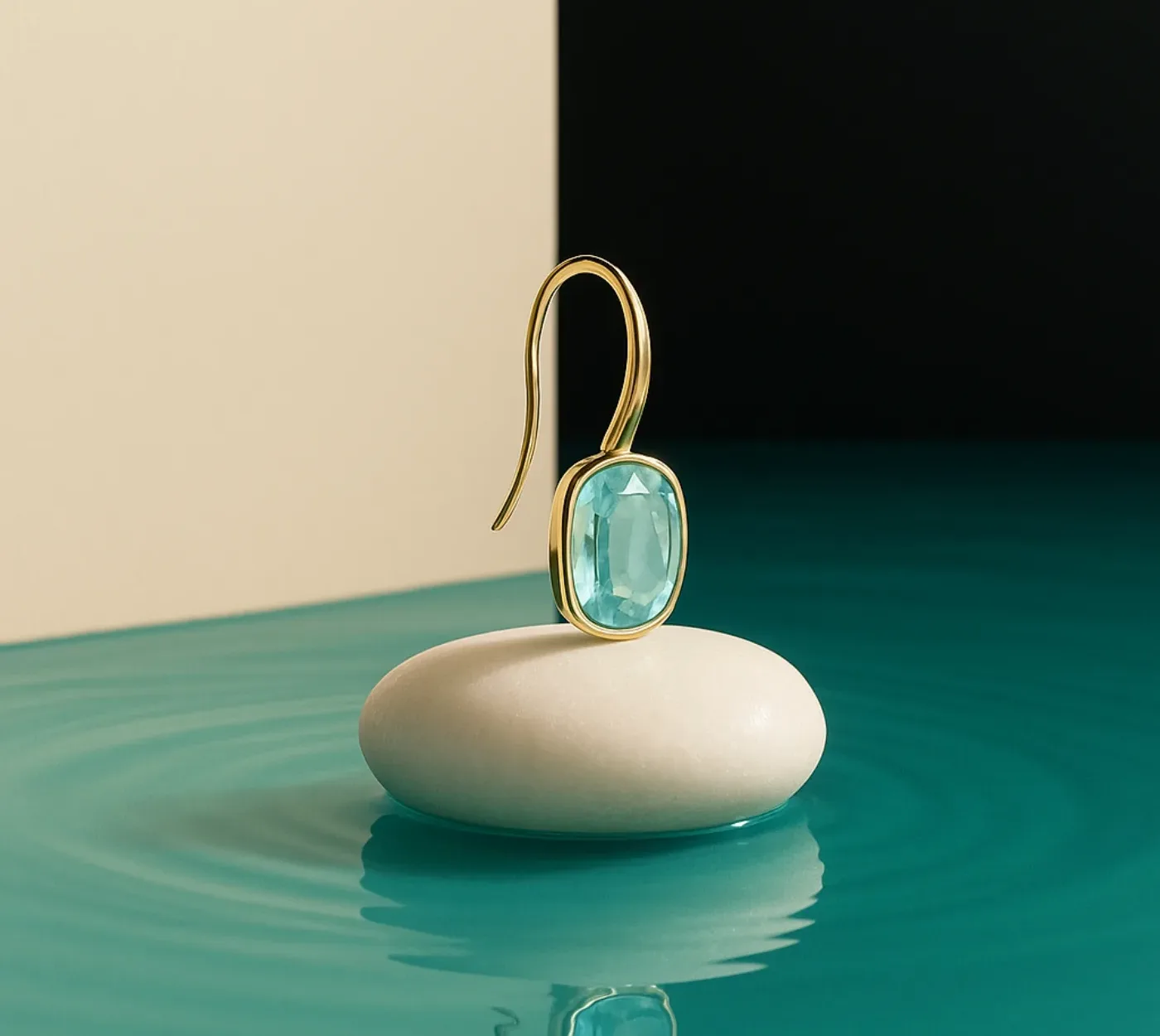 Orecchino in argento placcato oro 18KT con acquamarina, appoggiato su un ciottolo sull'acqua turchese