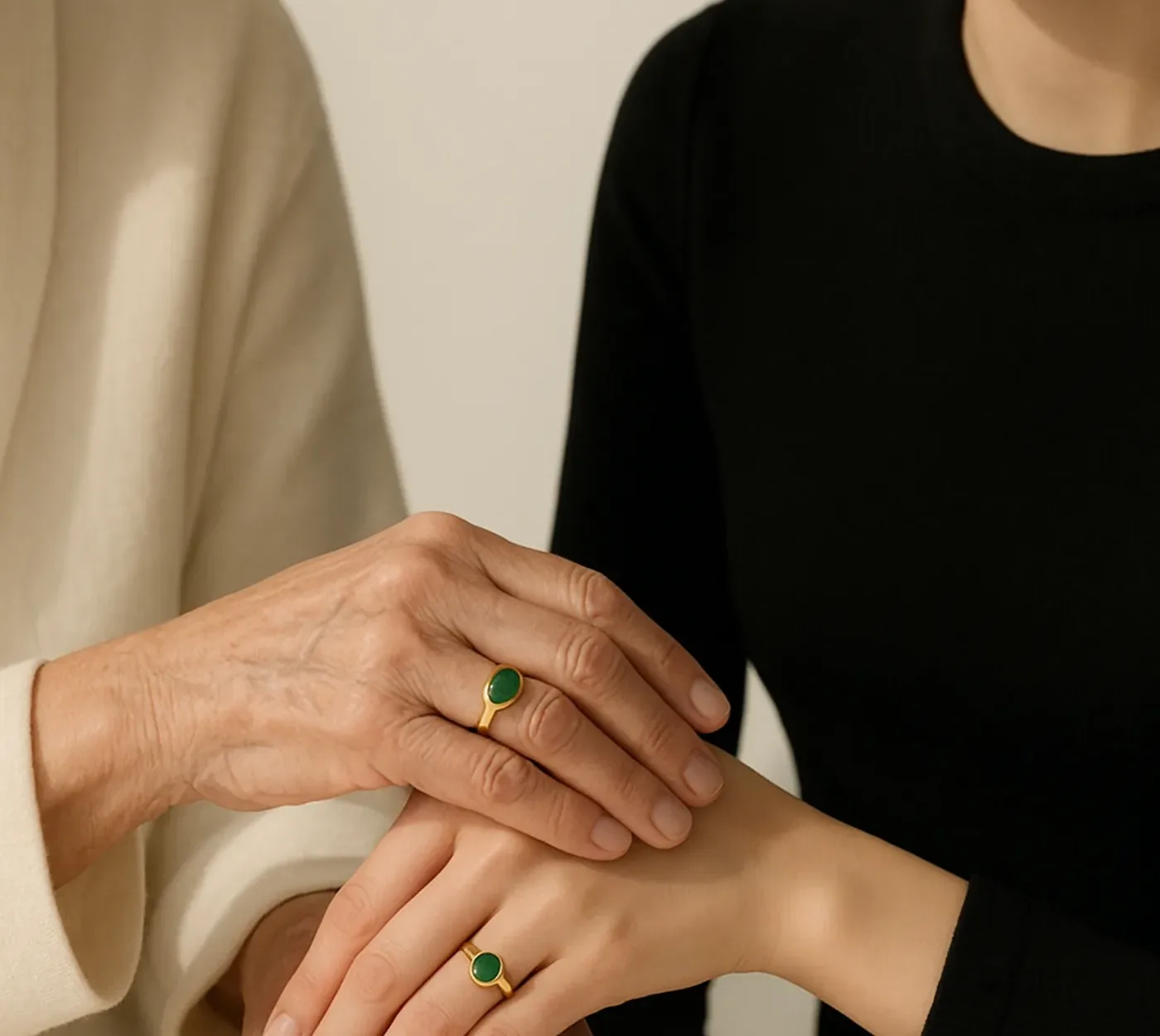 Le mani di due generazioni appoggiate una sull'altra, entrambe con un anello in oro e pietra verde